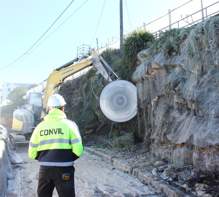 Image shows a site supervisor from convil group overseeing rock cutting with an excavator